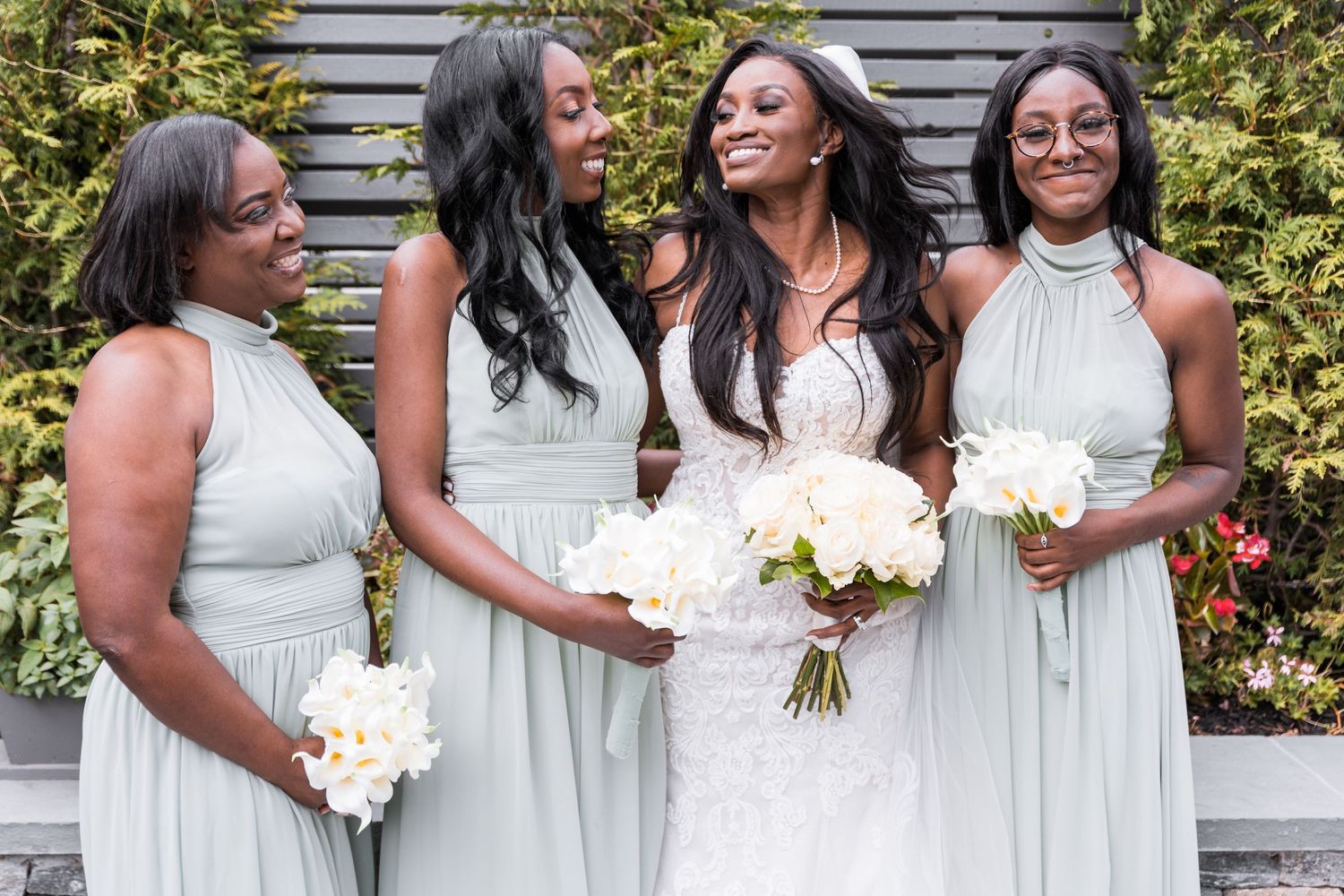 bridesmaids smiling at the bride in wedding dress while holding flowers at wedding