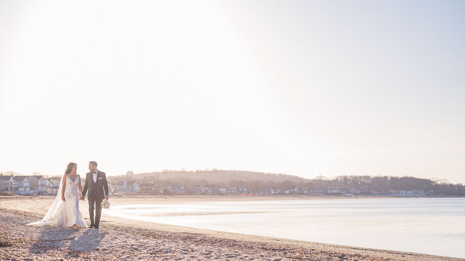 A couple walks alongside the water during a private moment between the groom and the bride at sunset.