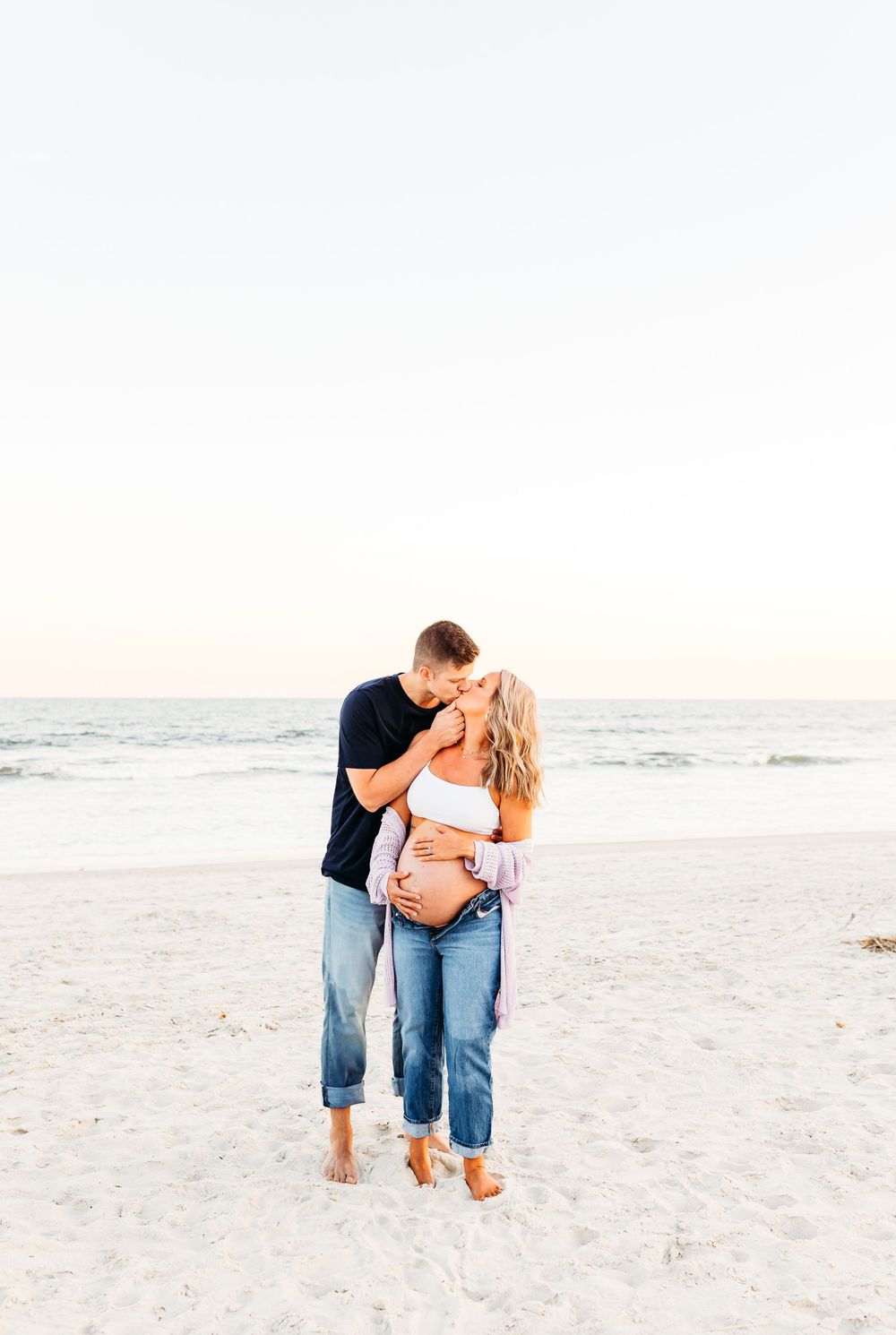 A romantic couple embraces on a serene white sandy beach at sunset during a photo session.