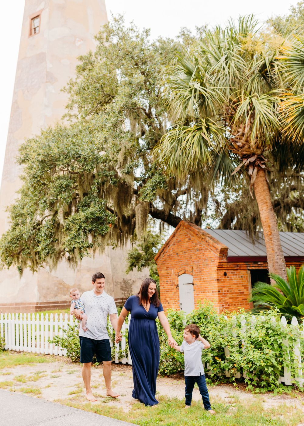 A couple and child walk along a scenic pathway with palm trees and brick buildings at a coastal location.