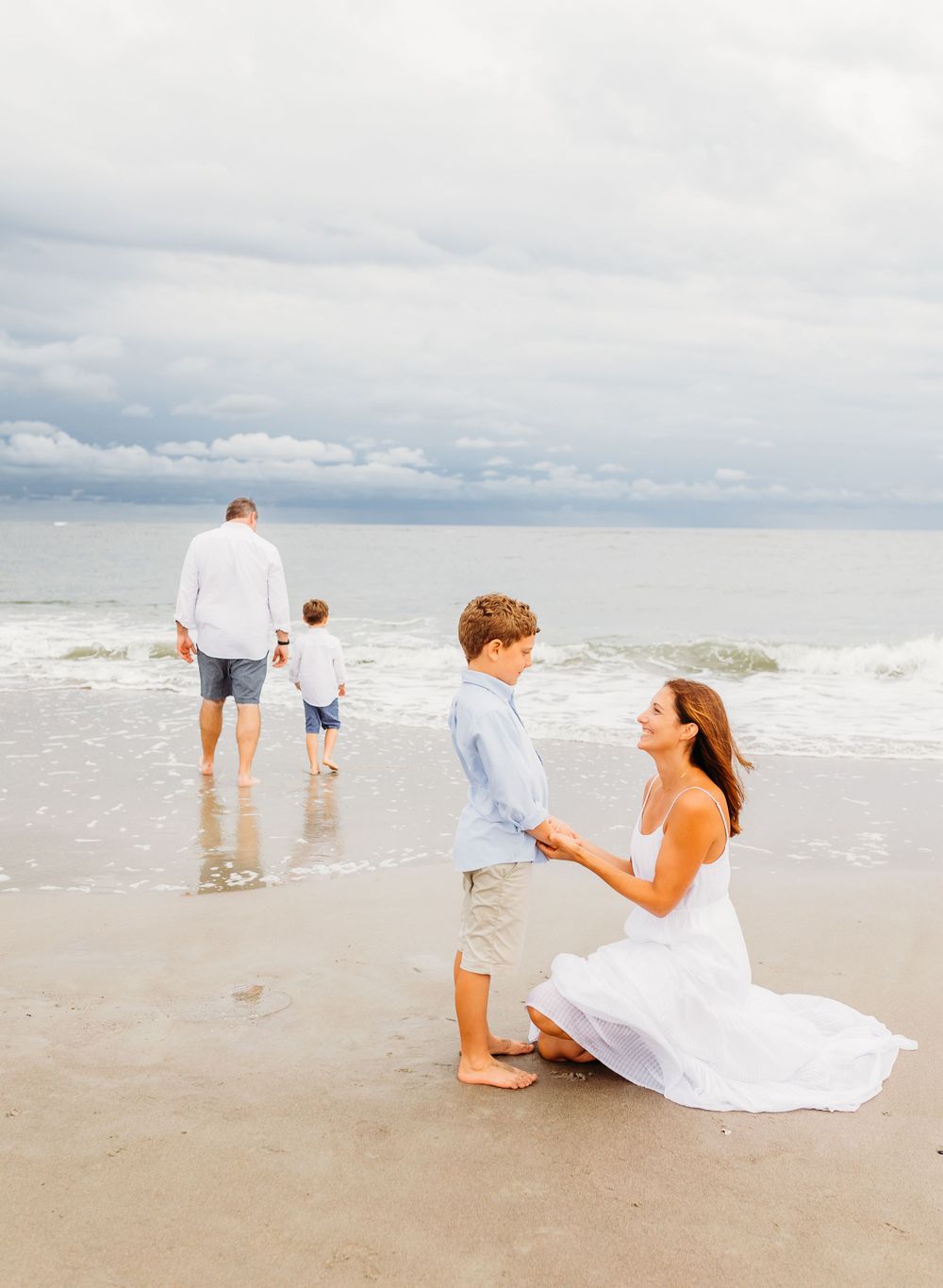 A couple enjoys a playful and romantic moment together on a cloudy beach with rolling waves in the background.