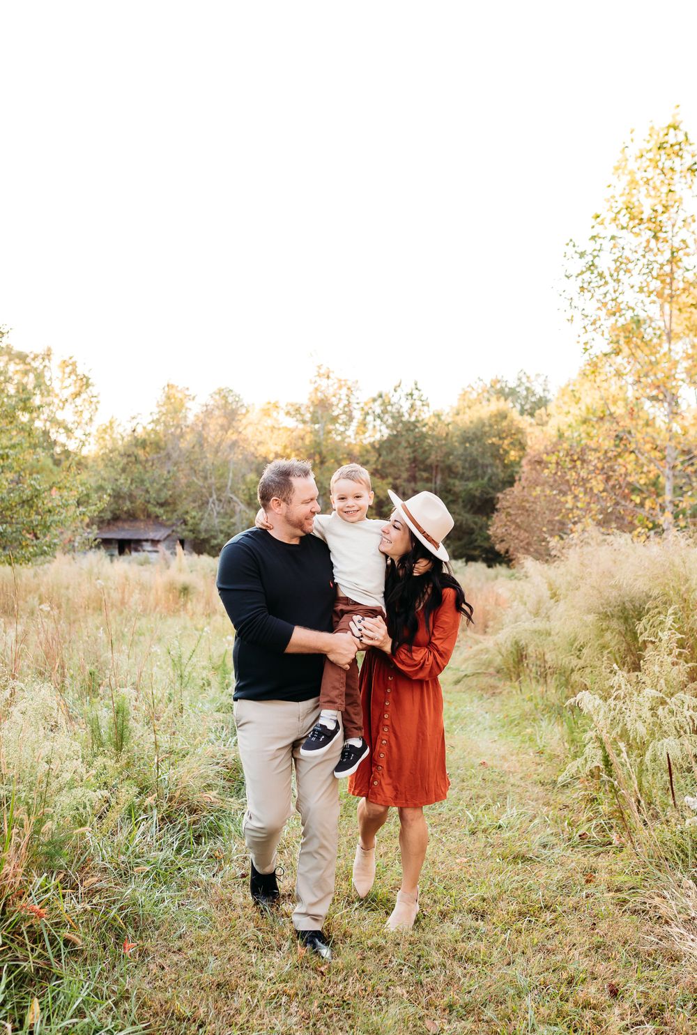 A family plays and laughs together in a sunlit field with tall grass during golden hour.