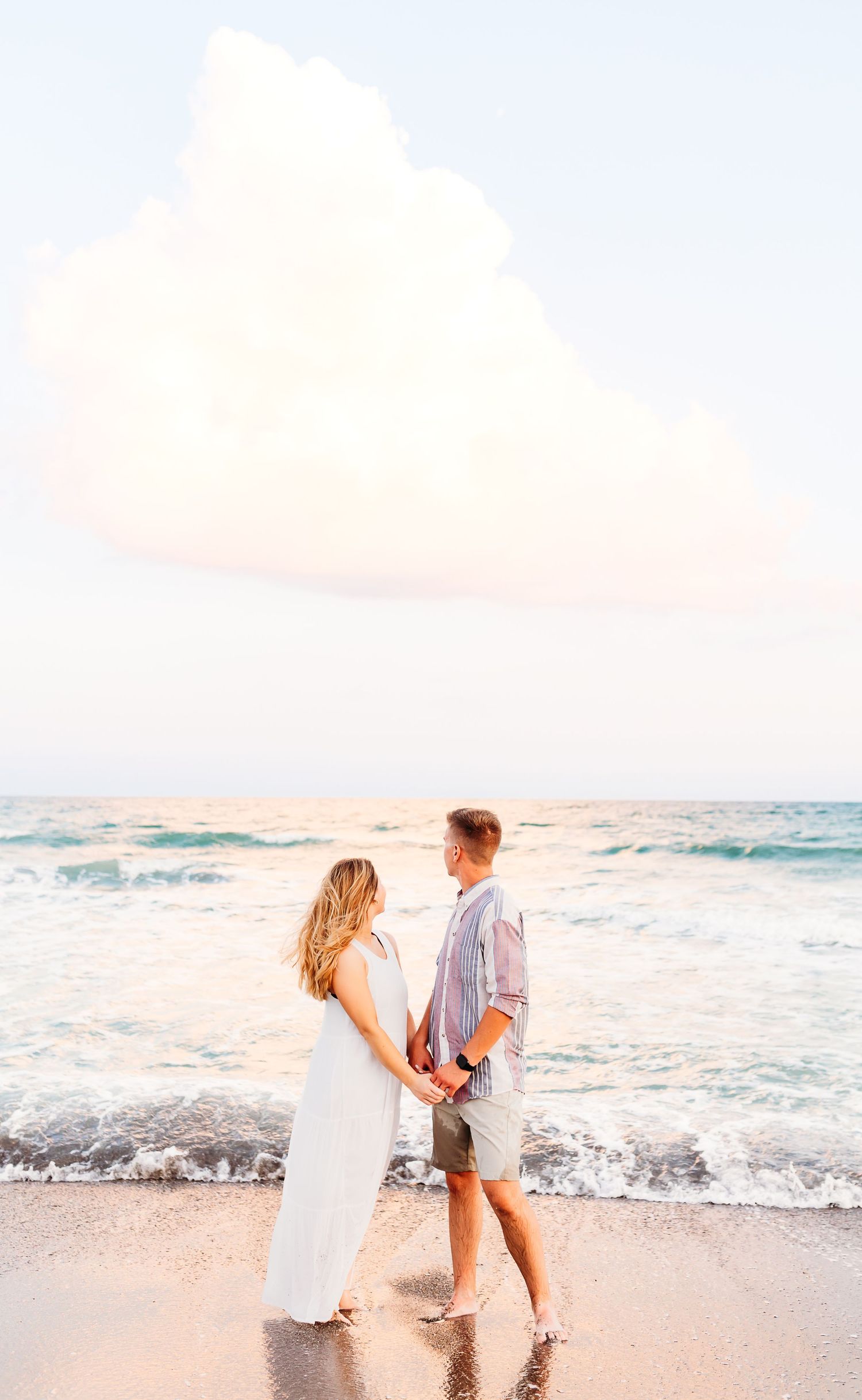 Couple playing and splashing in ocean waves at sunset with dreamy pink sky on tropical beach.