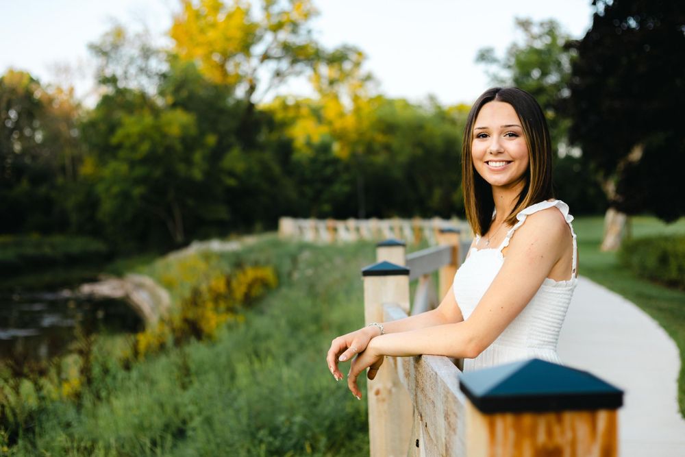 Woman leaning on wooden railing with yellow flowers and greenery in background.