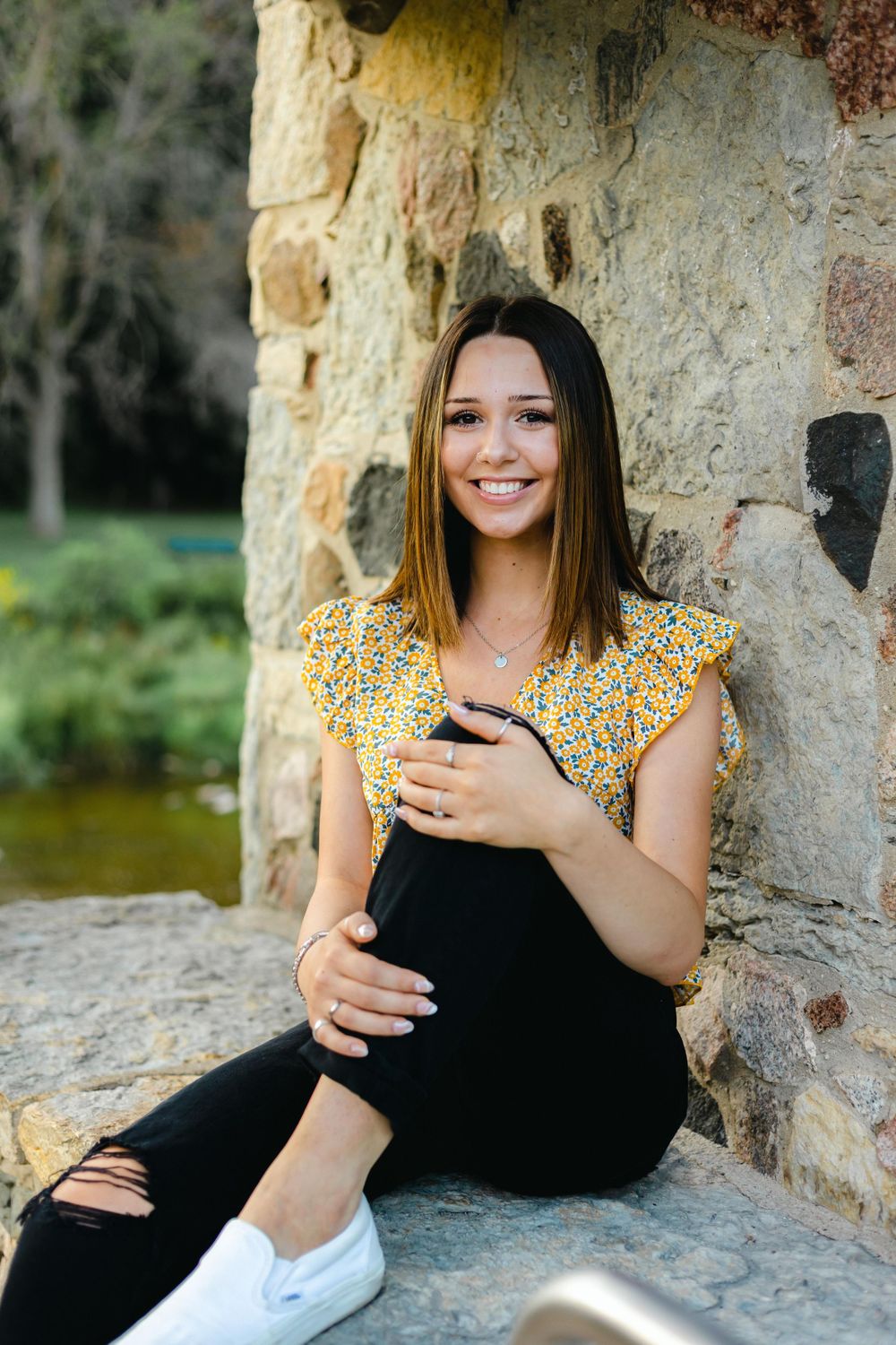 Portrait of woman in yellow top sitting against stone wall outdoors.