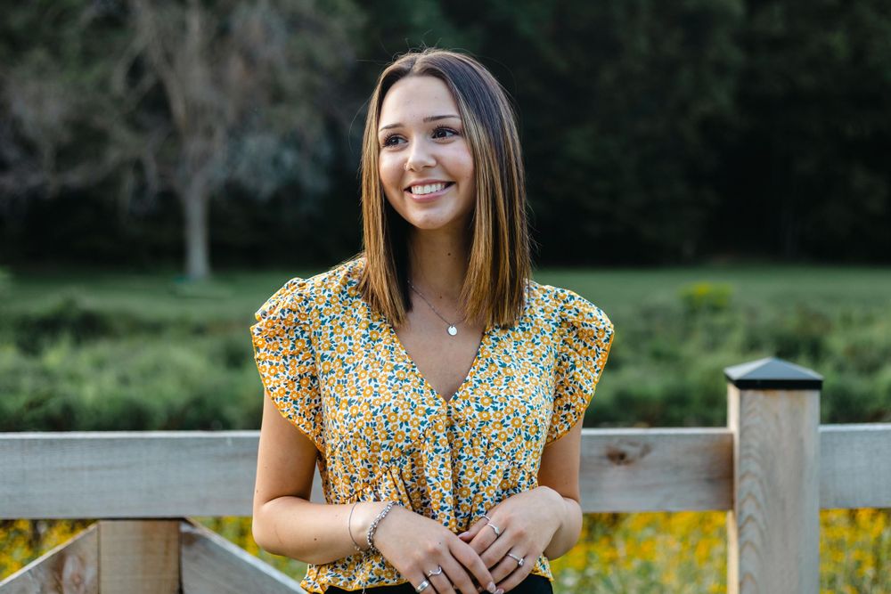 Portrait of woman in floral top standing on wooden deck with nature background.