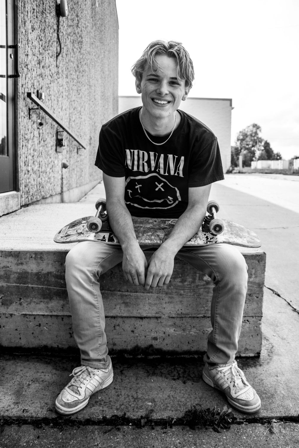 A skater sits on concrete steps wearing a Nirvana t-shirt and light-colored jeans.
