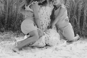 Candid black and white photo of family bonding on sandy dunes with beach fence.