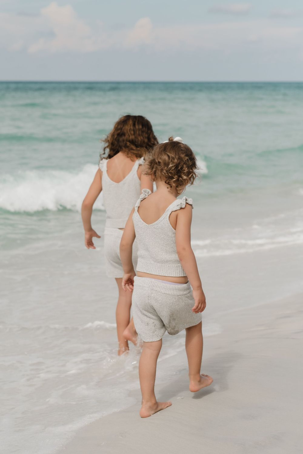 A parent and child walk together along the shoreline of a beach with turquoise waters.