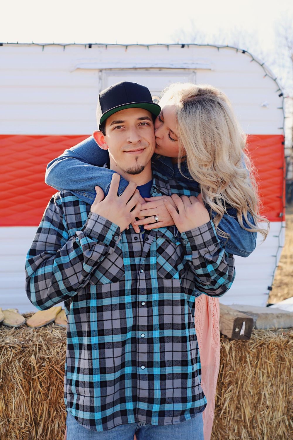 Couple sharing romantic moment against red and white barn backdrop.