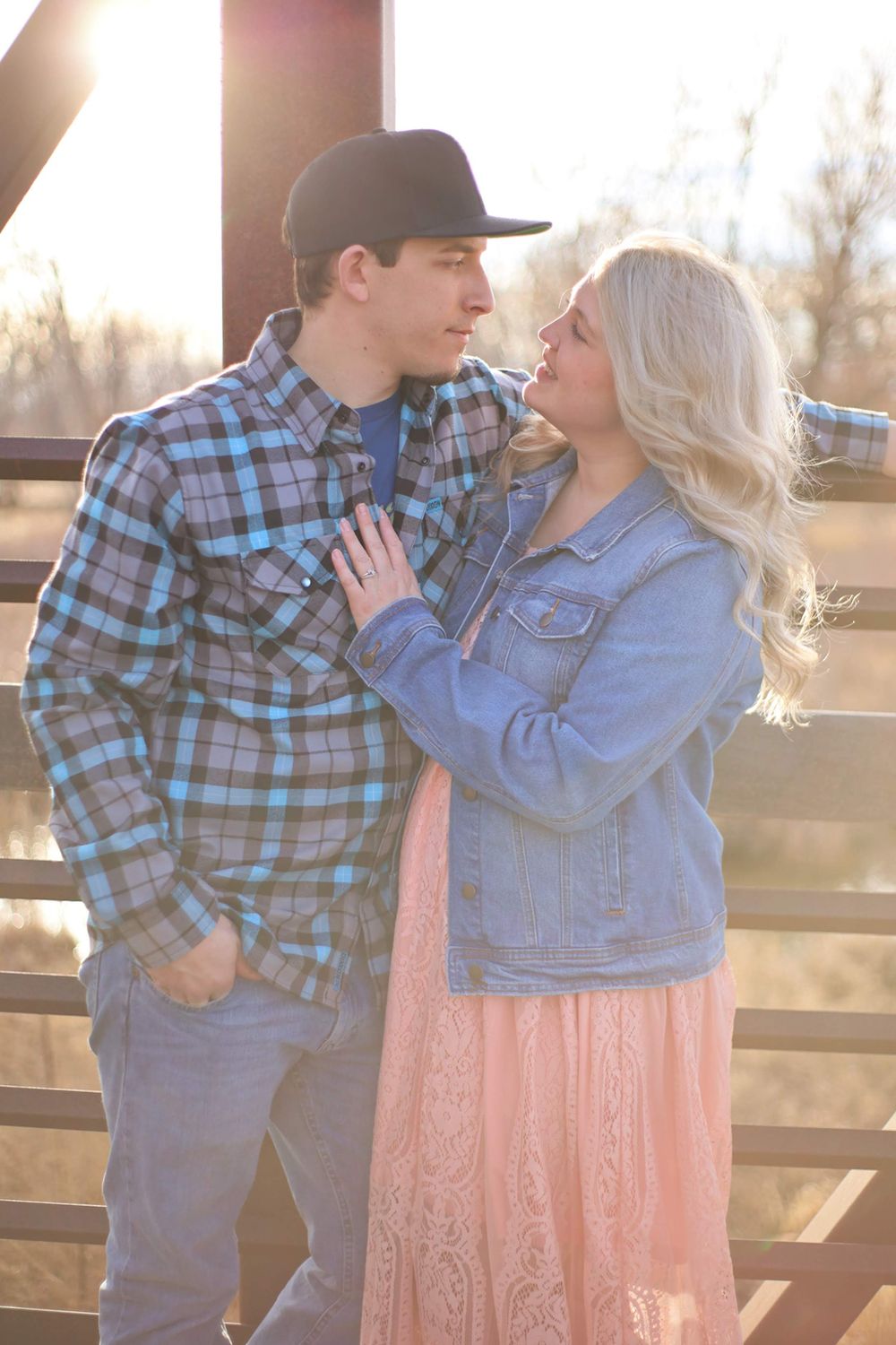Couple in denim and plaid embracing during golden hour by a wooden fence.