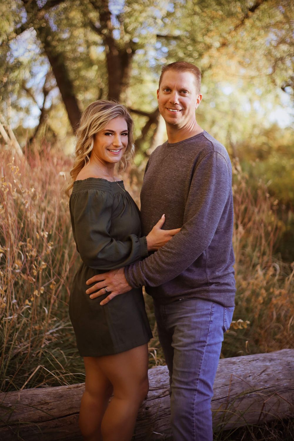 Romantic portrait of couple standing together in autumn field at sunset.
