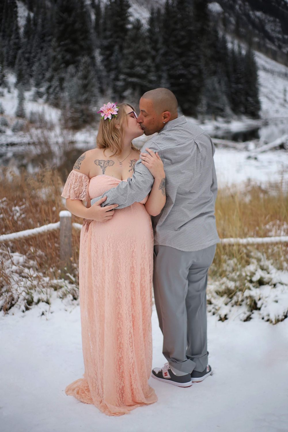 Couple embracing in snowy mountain landscape with woman wearing long pink dress.