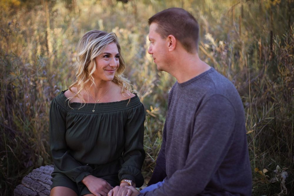 Couple having intimate conversation while sitting in tall grass during golden hour.