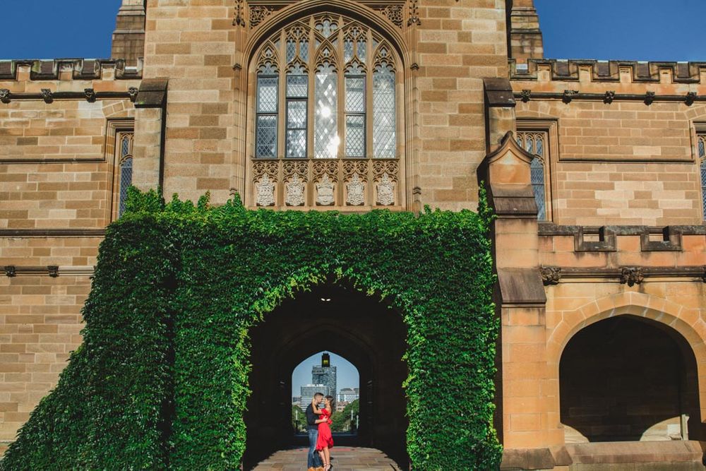 A red dress stands out against sandstone architecture and ivy-covered walls.