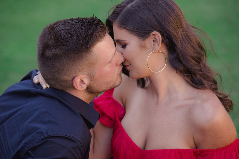 Romantic outdoor photo session with red dress against green garden background.