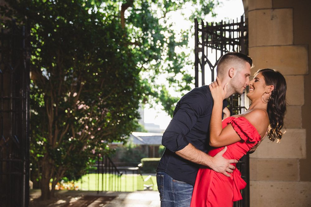 Couple shares intimate moment under stone archway with natural lighting.