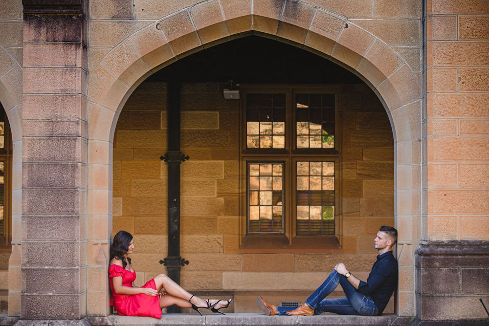 A romantic couple embraces in an elegant stone archway corridor with warm lighting and architectural details.