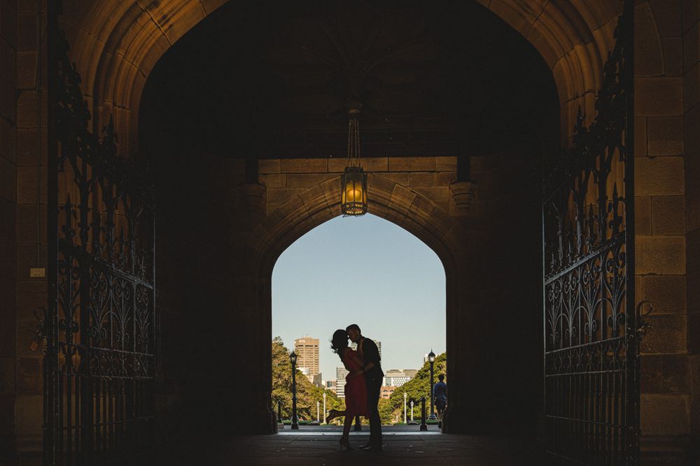 A silhouetted couple embraces in a dramatic stone archway with bright background.