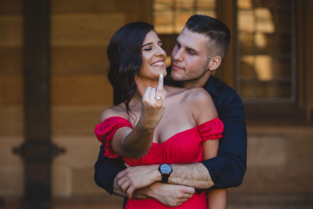 A couple shares an intimate moment in a historic stone hallway with arched windows and columns.