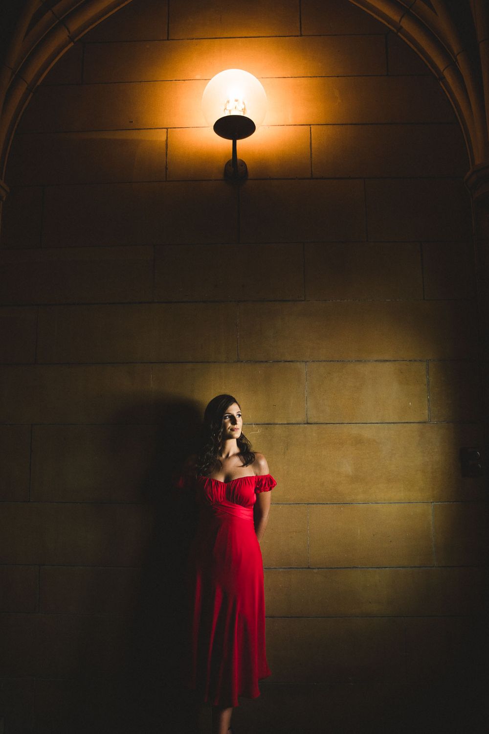 Dramatic lighting illuminates figures in red and black against a stone wall with arched architecture.