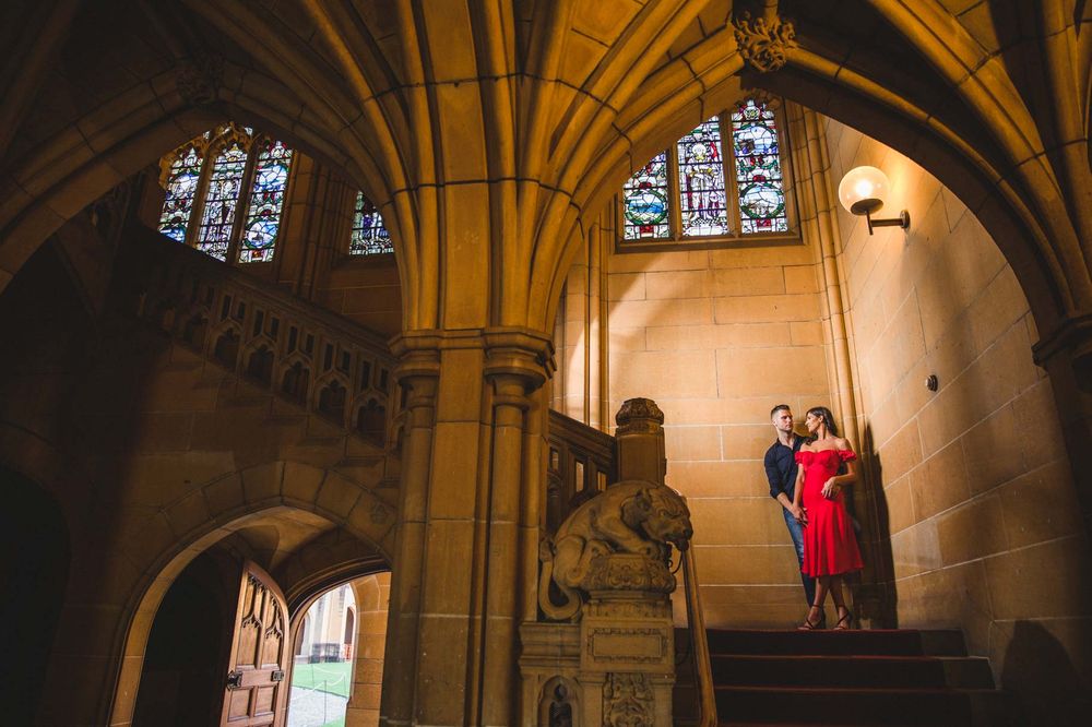 A couple stands beneath Gothic arches and stained glass windows in a historic building.