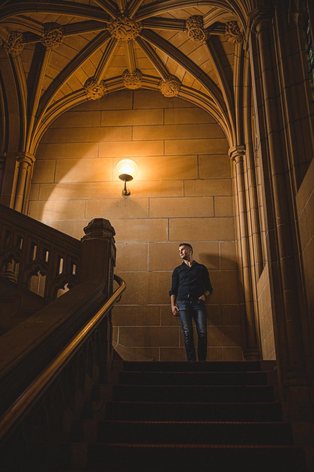 A dramatic architectural photo showing Gothic vaulted ceilings and stone staircases with moody lighting.