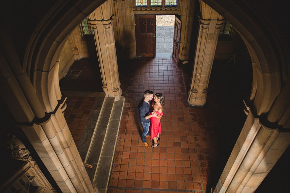 An aerial view of figures in a Gothic cathedral corridor with dramatic lighting and stone archways.