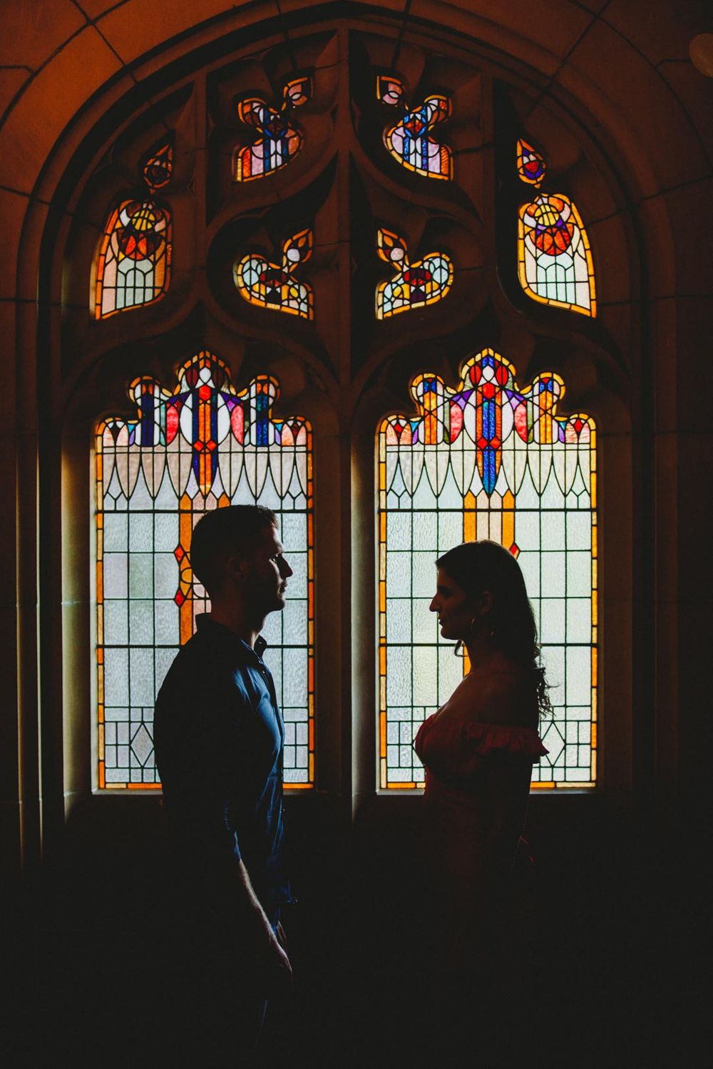 Silhouettes against stained glass windows in a gothic cathedral create a dramatic backlit effect.
