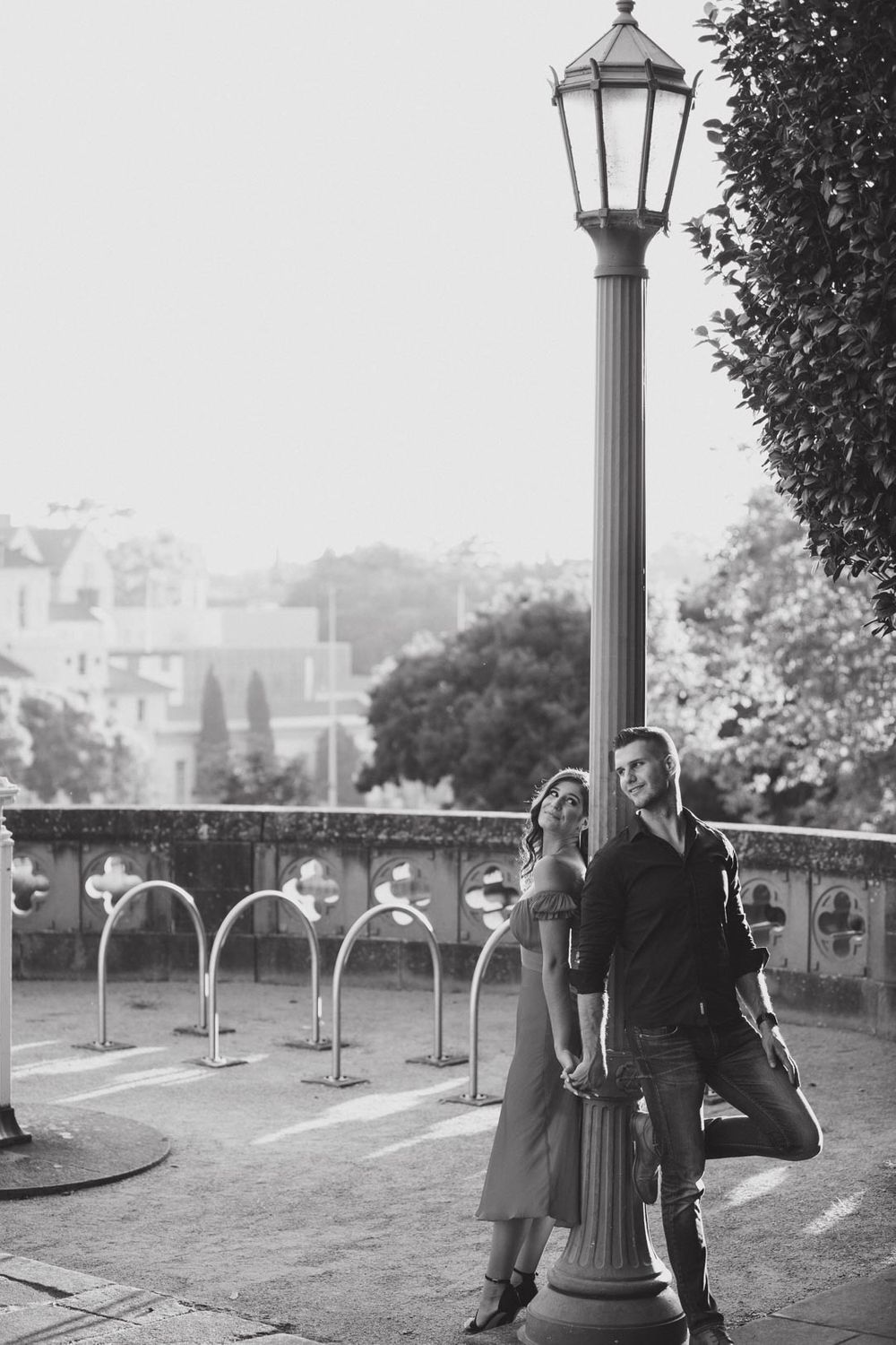 A black and white photo of people standing near vintage lampposts on a terrace overlooking a city.