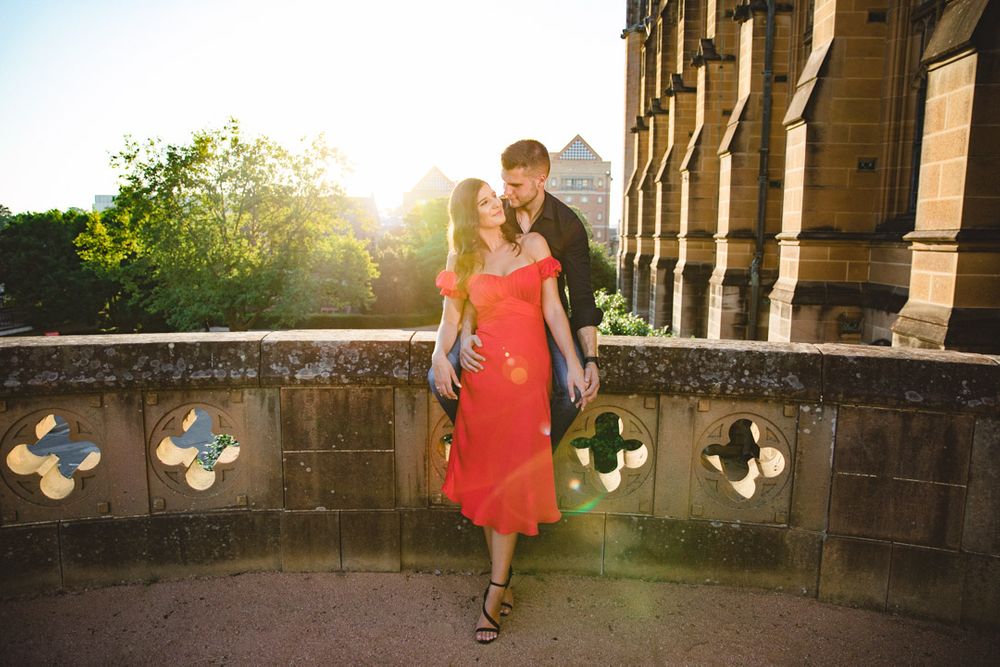 A couple walks along a stone terrace during golden hour, creating long shadows.