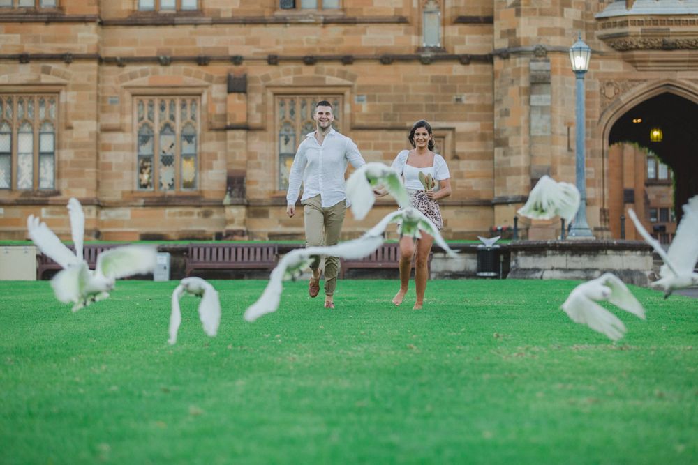 People walking on grass near historic stone buildings with gothic architecture.