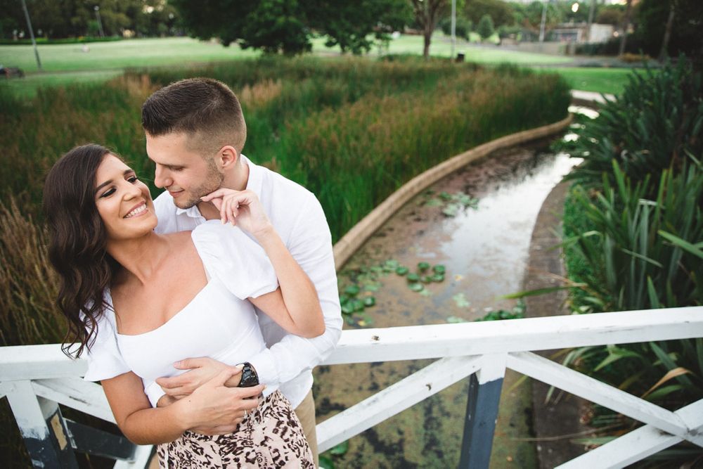 A couple shares intimate moments along a white fence near a garden path.