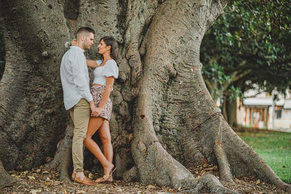 A couple shares an intimate moment against the massive trunk of an ancient tree.
