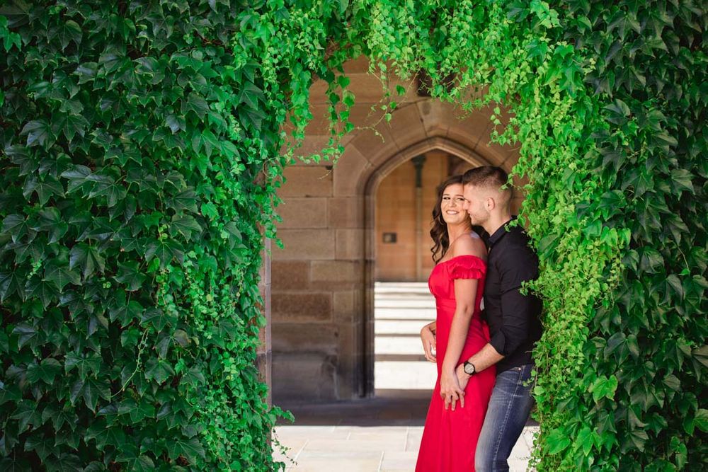 A romantic moment in an ivy-covered stone archway with gothic architectural details.
