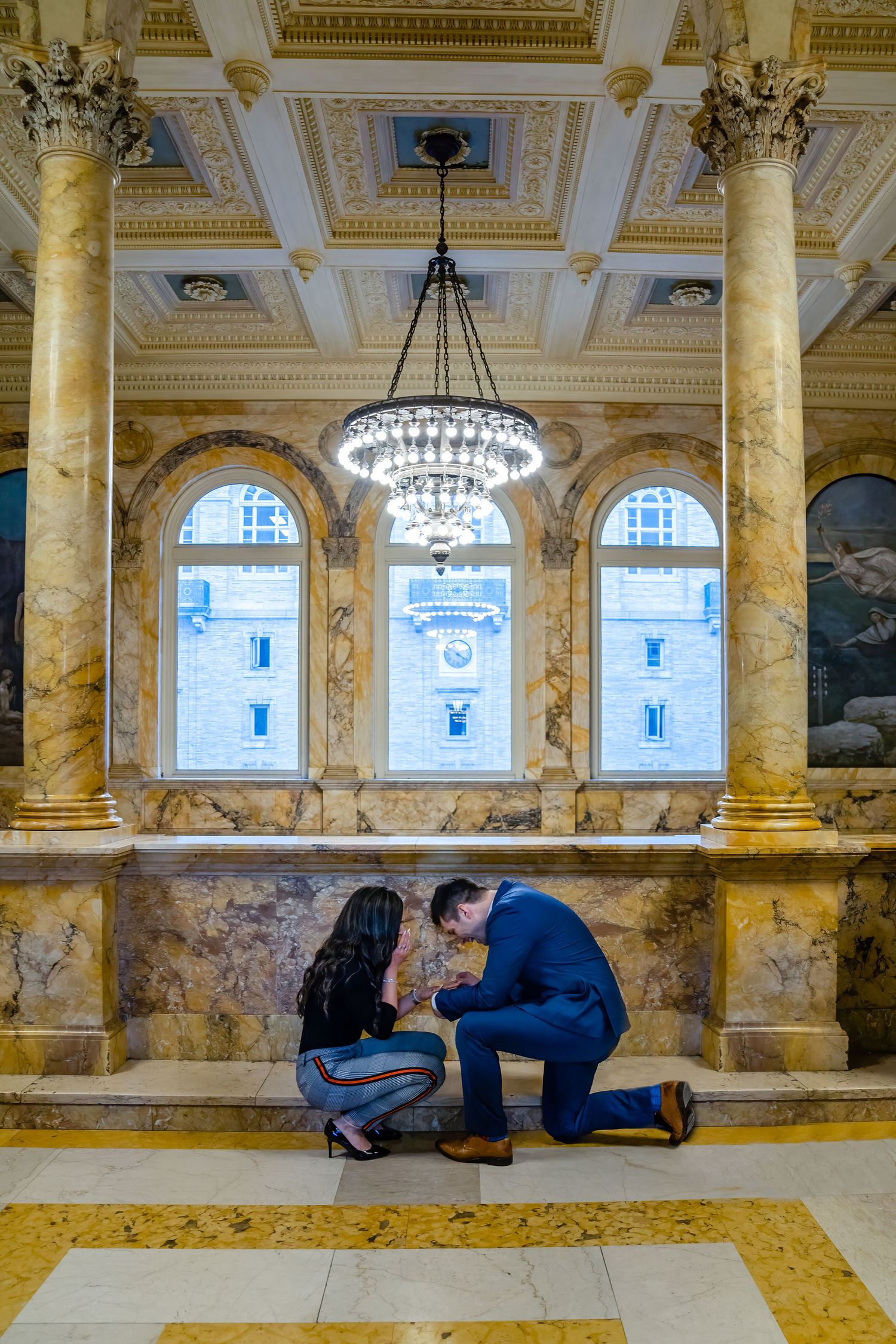 A special moment captured in a grand marble hallway with classical architecture and chandelier.