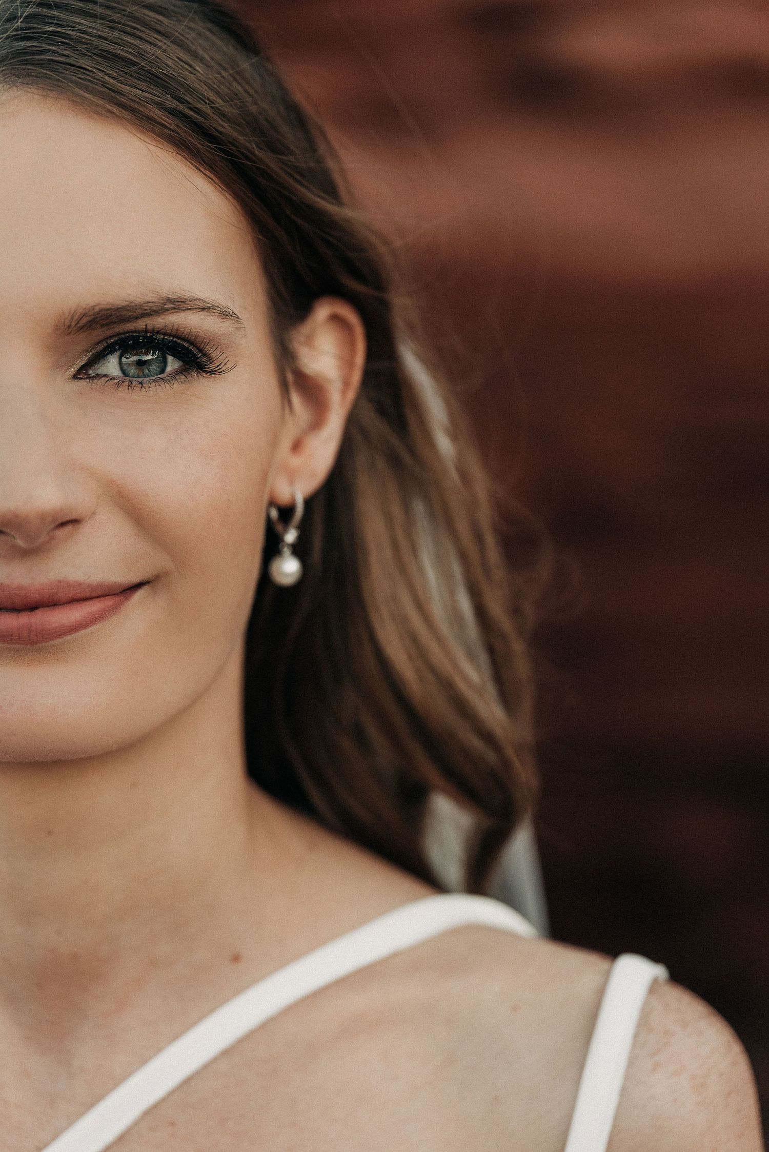 Portrait featuring soft lighting and elegant pearl drop earrings against a blurred rustic background.