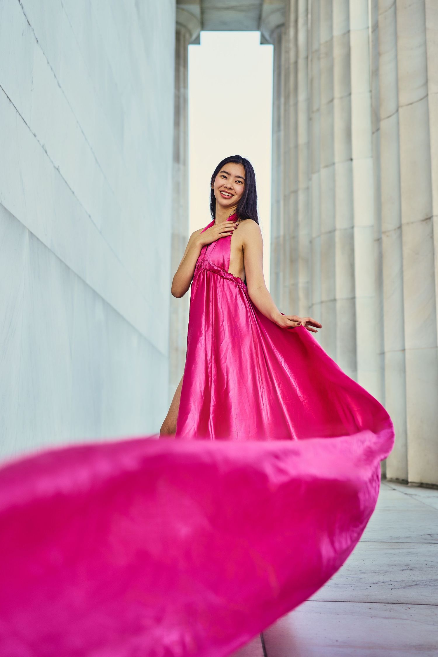 Flowing hot pink silk dress billows dramatically between classical marble columns.