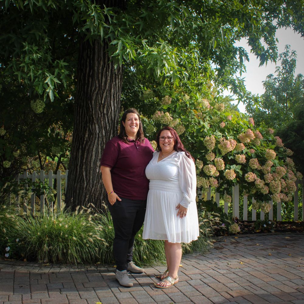 A couple poses in a garden setting with lush greenery and hydrangea bushes behind them on a brick patio.