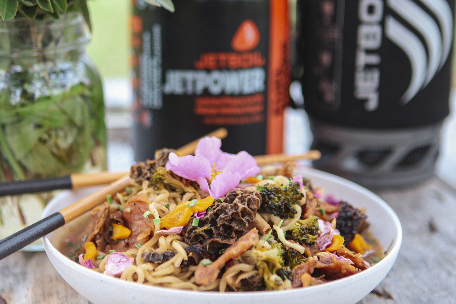 Asian noodle bowl with colorful toppings and garnishes served alongside beverages.