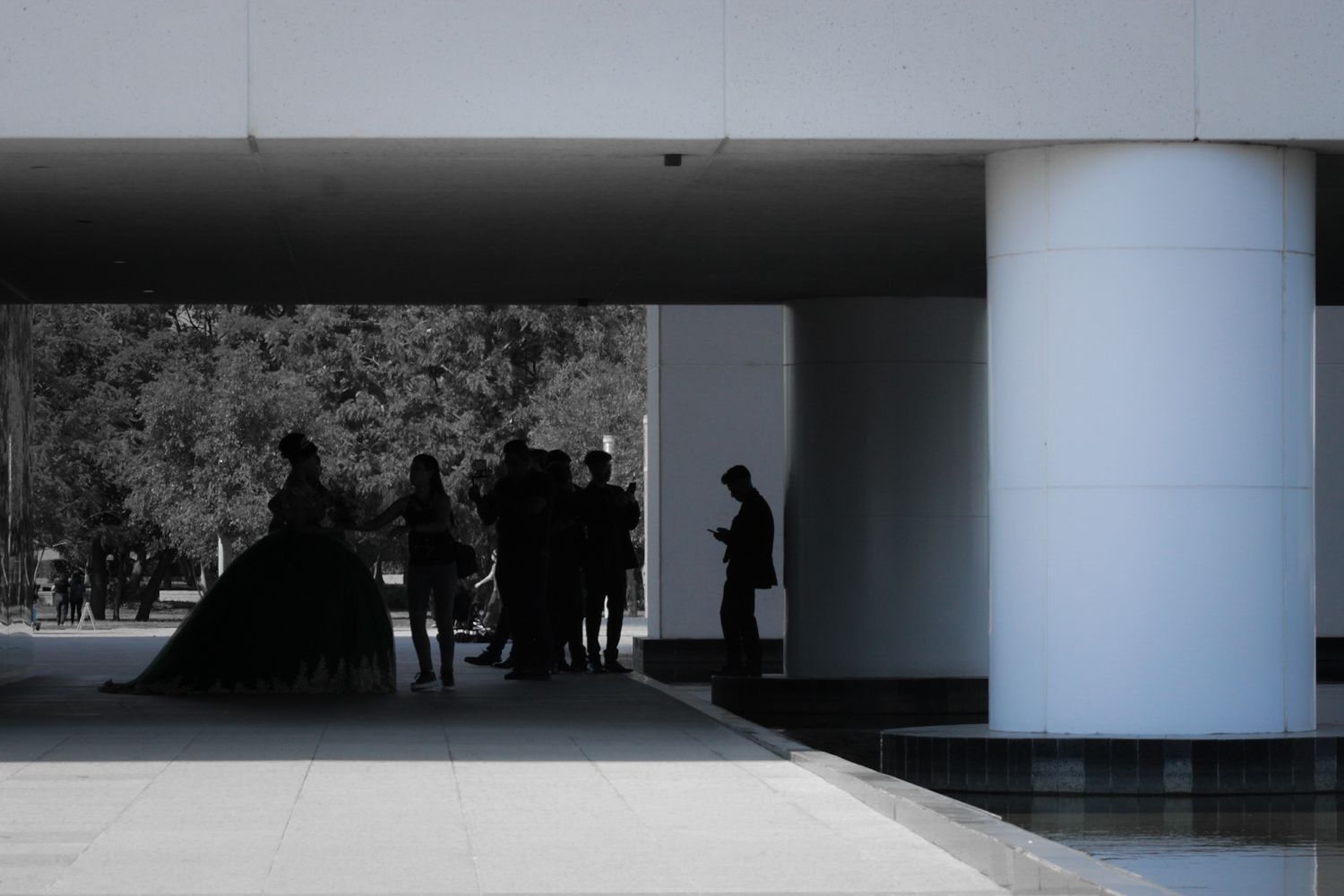 Black and white silhouette of people gathered under a modern building overhang.