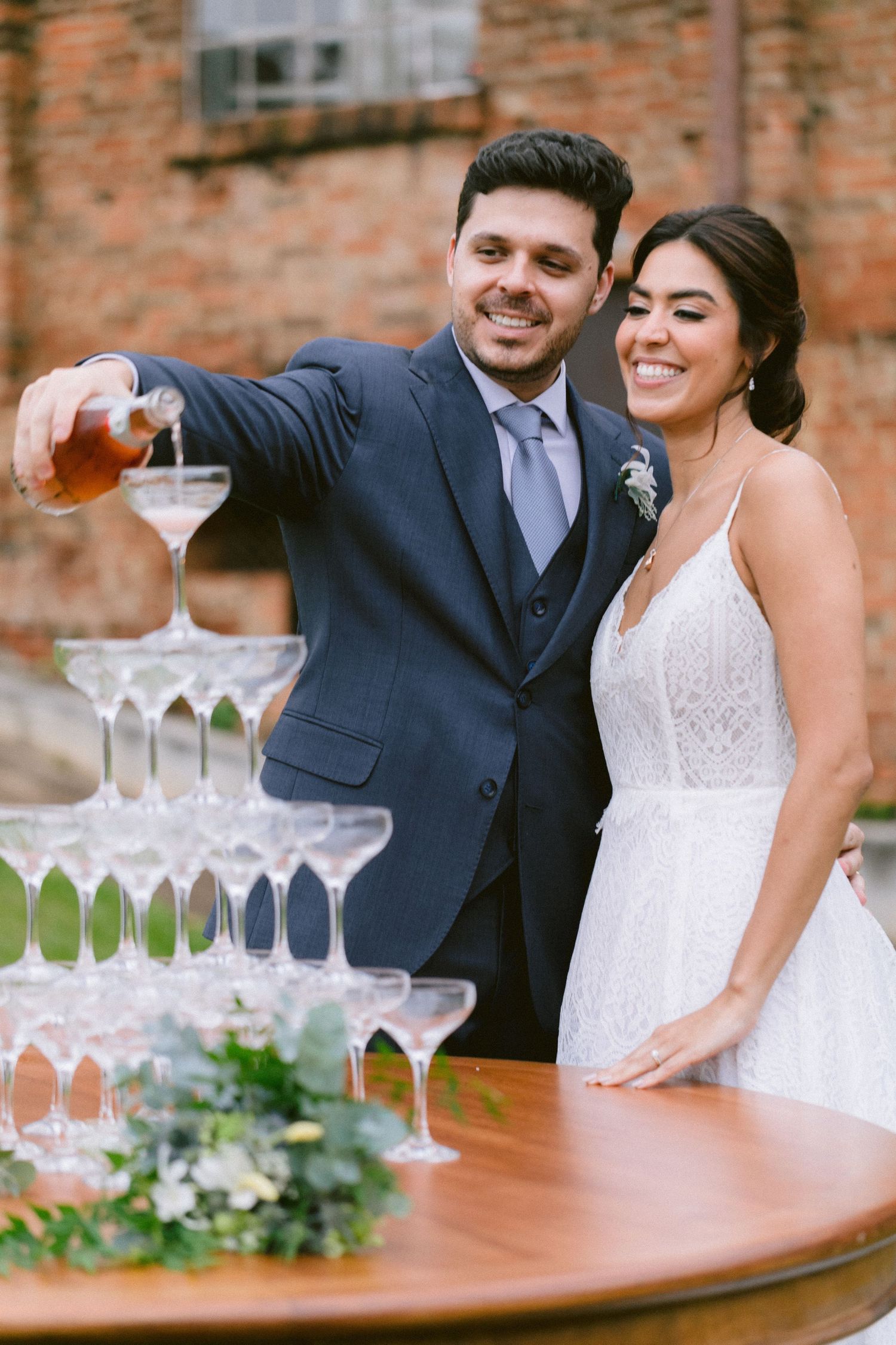 Couple pouring champagne into tower of glasses at wedding reception.