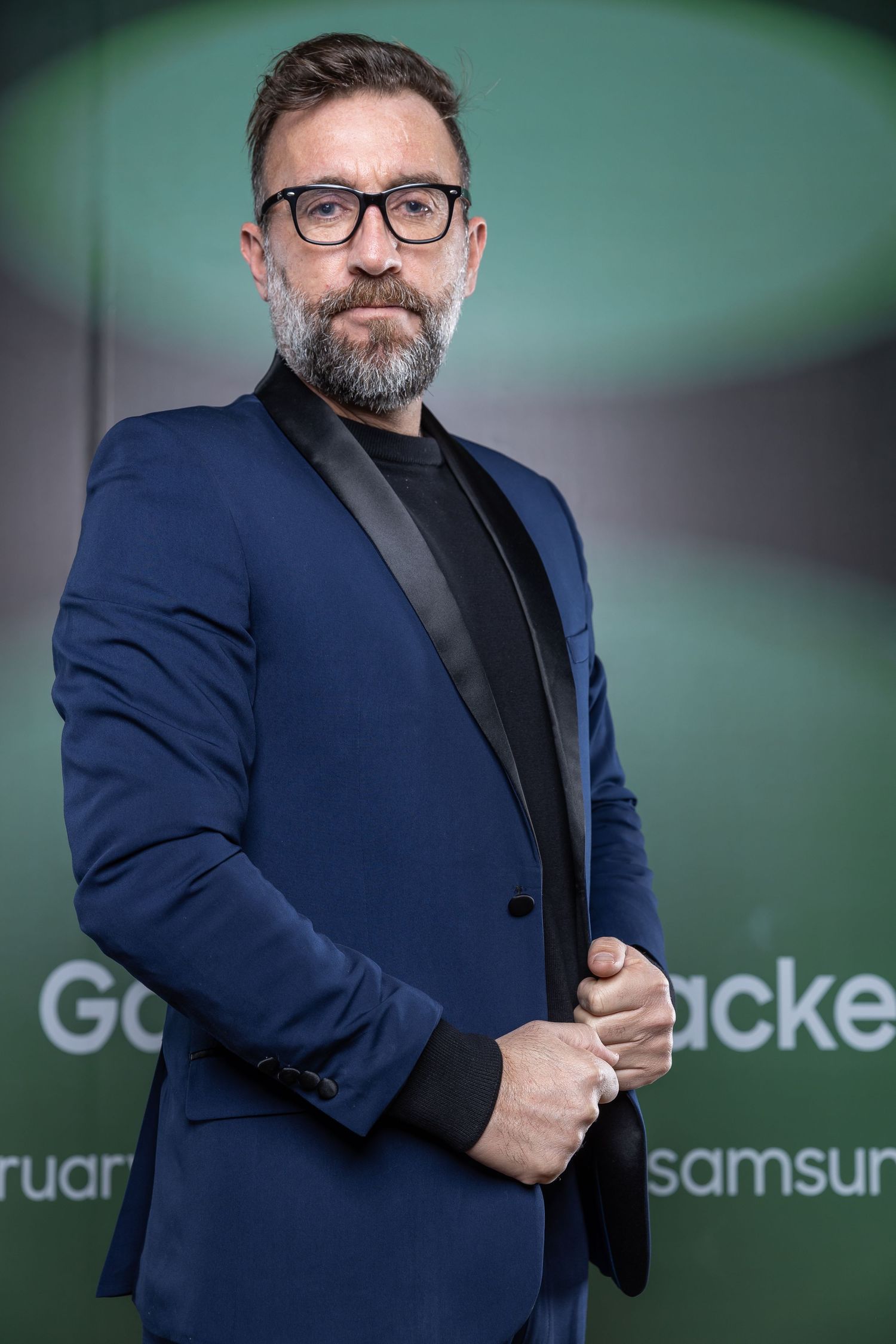 Professional in navy blazer and glasses posed against green backdrop at Samsung event.