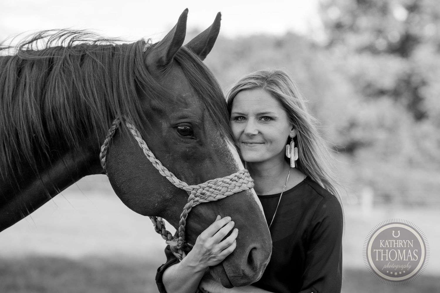 Close-up black and white portrait of brown horse with braided halter in natural setting.