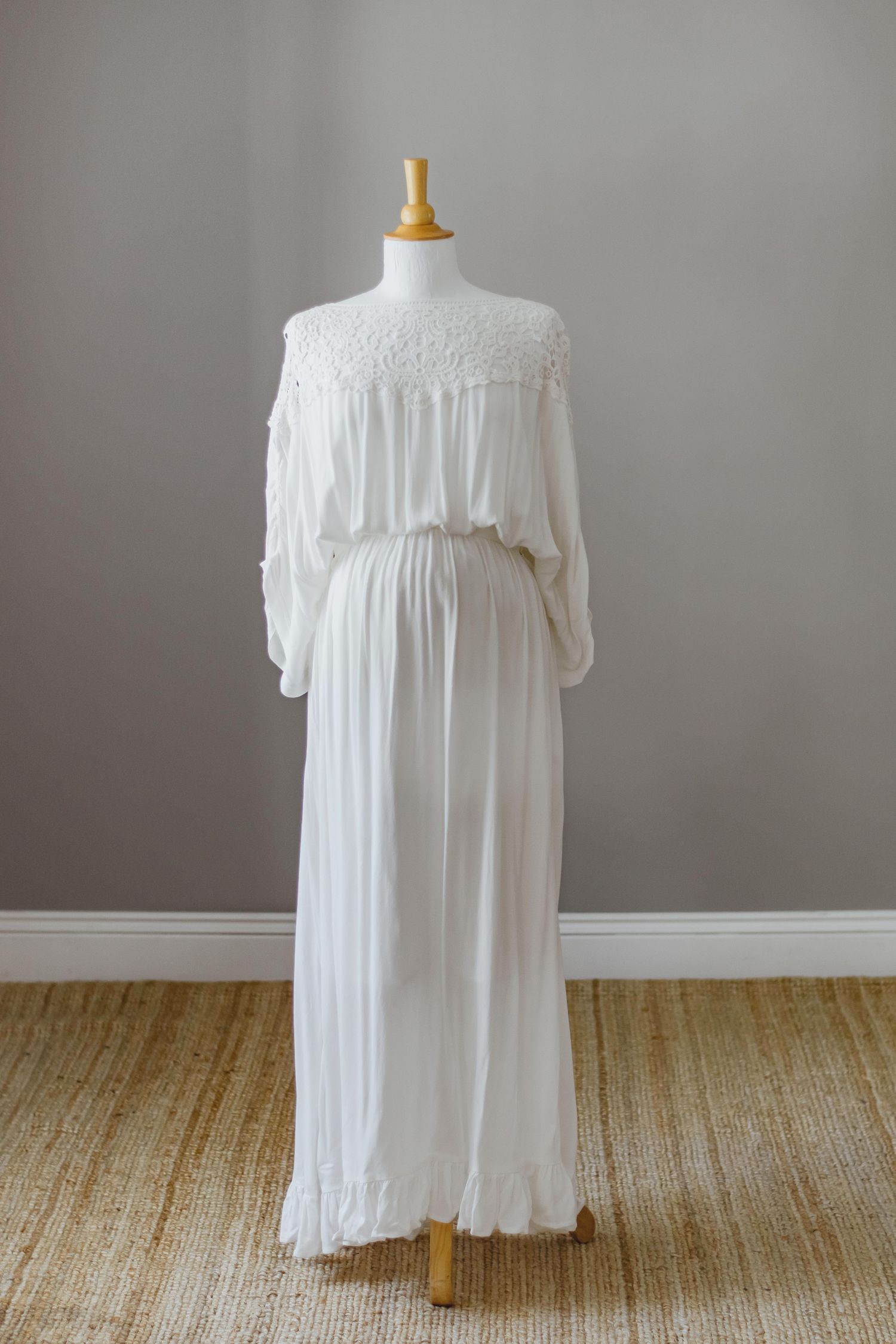 Elegant white lace maternity dress on mannequin with flowing fabric and high neckline.