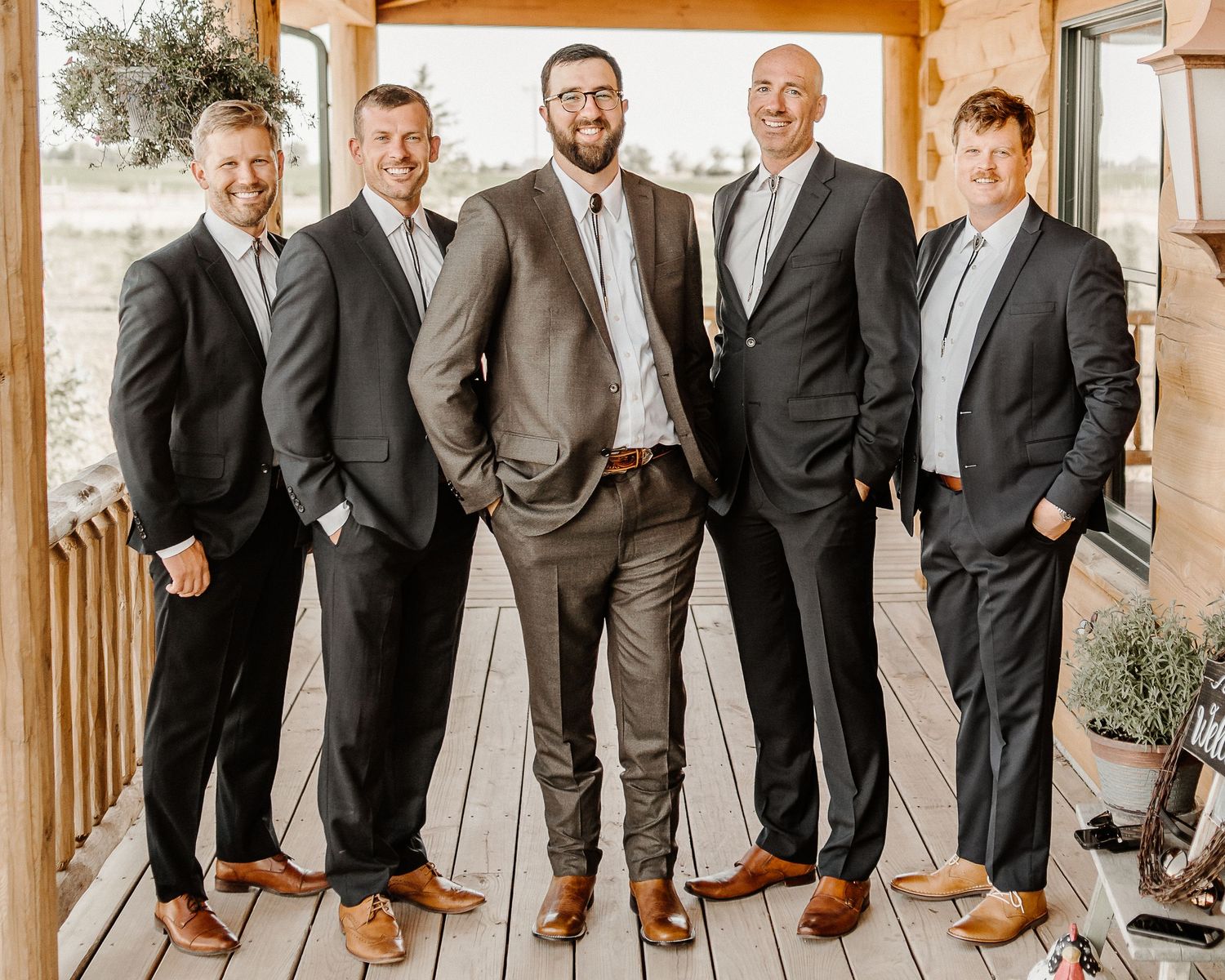 A group of well-dressed people in suits standing together on a porch with warm lighting and rustic decor.
