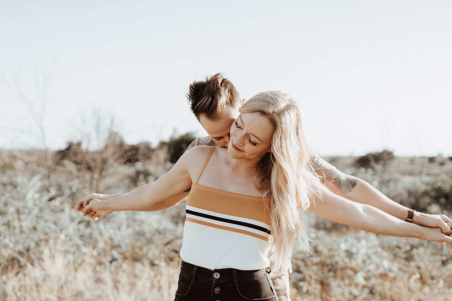 A joyful couple embraces while standing in a natural desert landscape during golden hour.