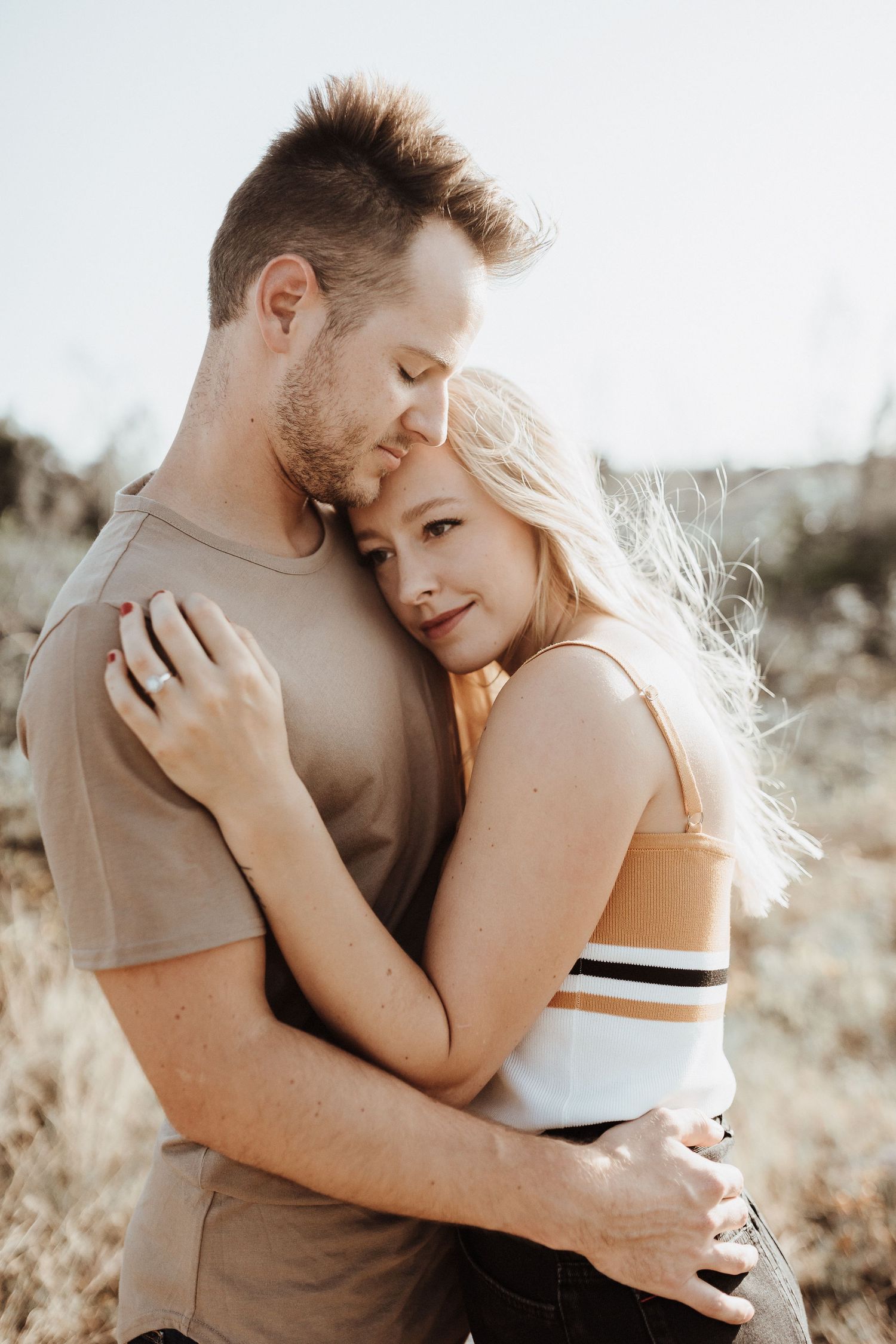 A romantic embrace between couple in golden sunlight with her blonde hair glowing in nature setting.
