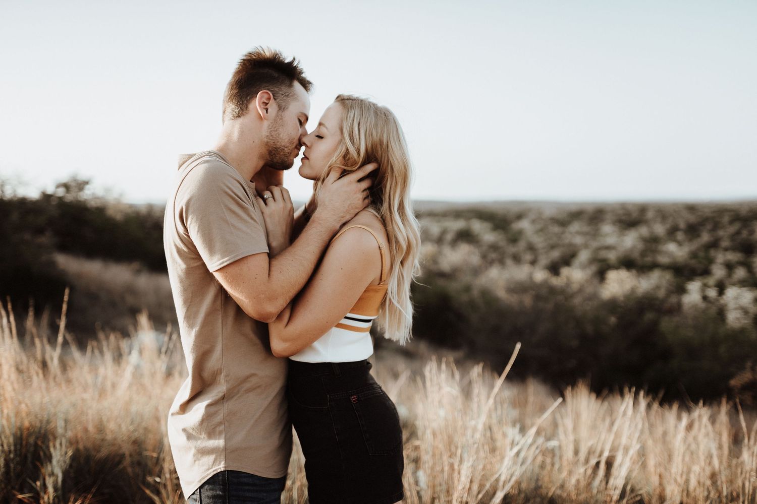 A romantic couple shares an intimate moment while standing in a golden field during sunset.