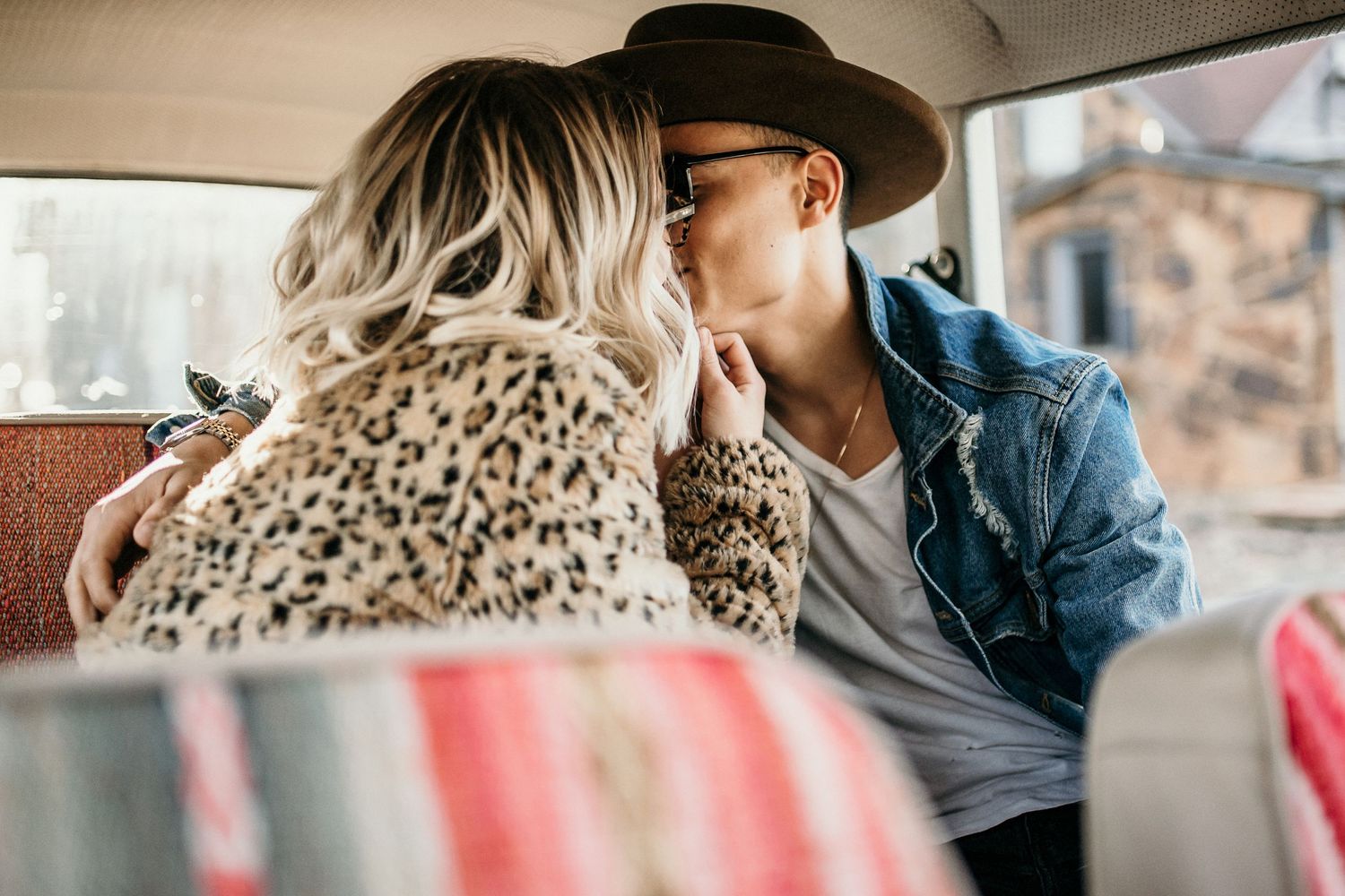 Romantic couple sharing intimate moment in vintage car backseat with leopard print and denim clothing.